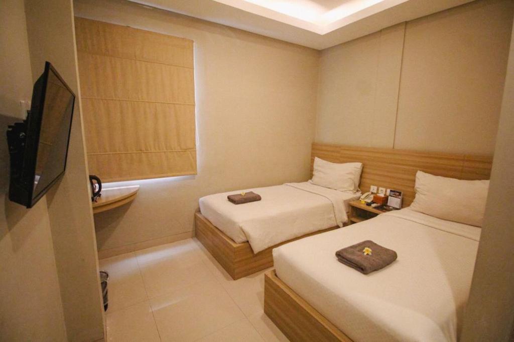 a small room with two beds and a television at Kuta Majesty Hotel in Legian