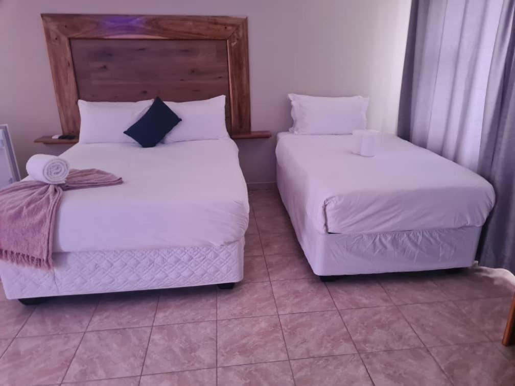 two beds in a room with white sheets and pillows at The Botanical Gardens in Rundu