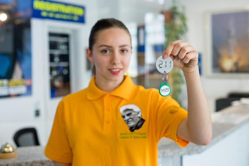 a woman in an orange shirt holding up a key at Space Hotel im Campus der JvP Schule in Leipzig