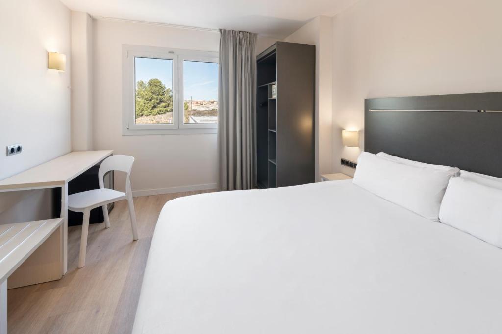 a white bedroom with a bed and a desk and a window at B&B HOTEL Barcelona Rubí in Rubí