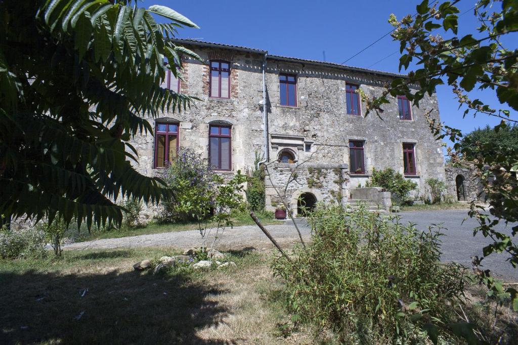 uma antiga casa de pedra com janelas vermelhas num quintal em Logis de Riparfonds em Bressuire