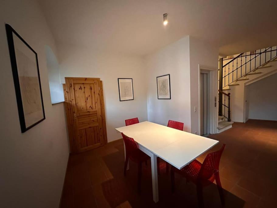 Rancate charme apartment في منديريسو: غرفة طعام مع طاولة بيضاء وكراسي حمراء