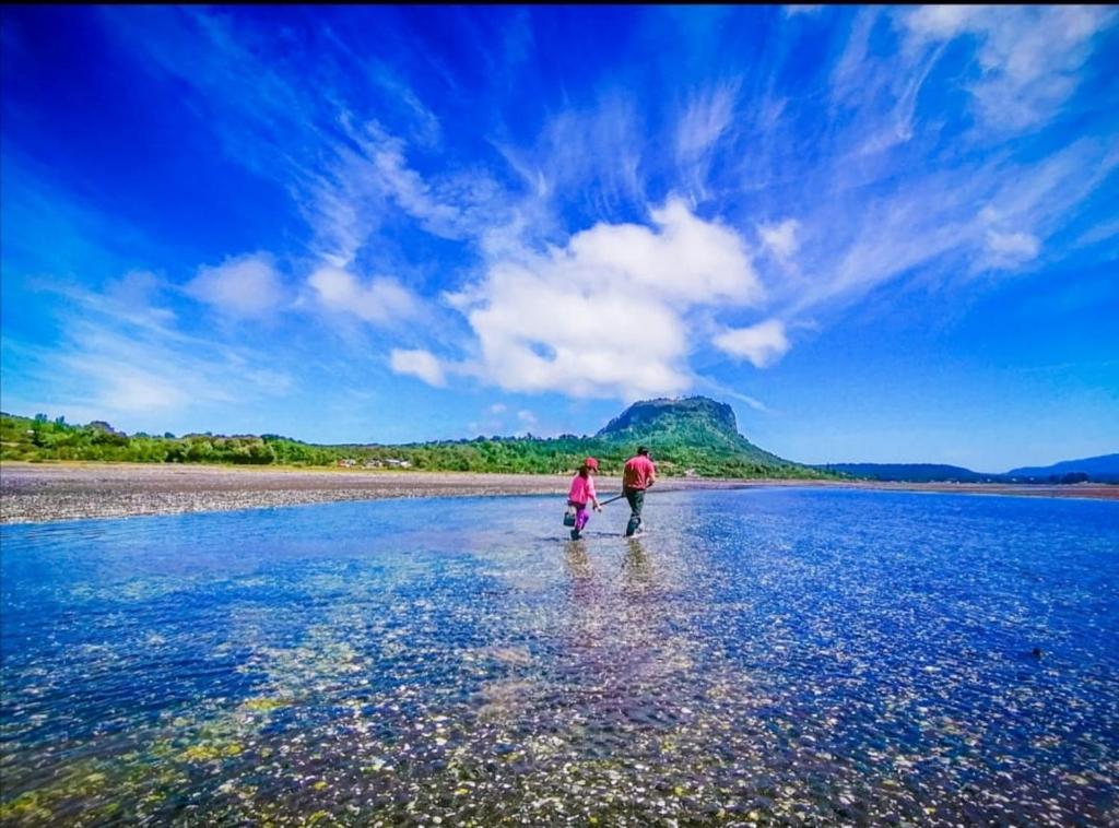 dos personas caminando sobre el agua en una playa en CABAÑA HUALAIHUE AUSTRAL, en Hornopirén