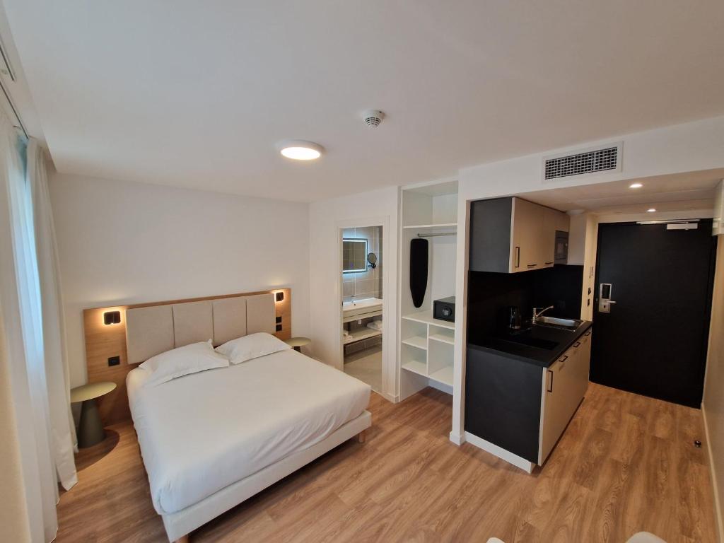 a bedroom with a white bed and a kitchen at Appart'hôtel Marianne in Montpellier