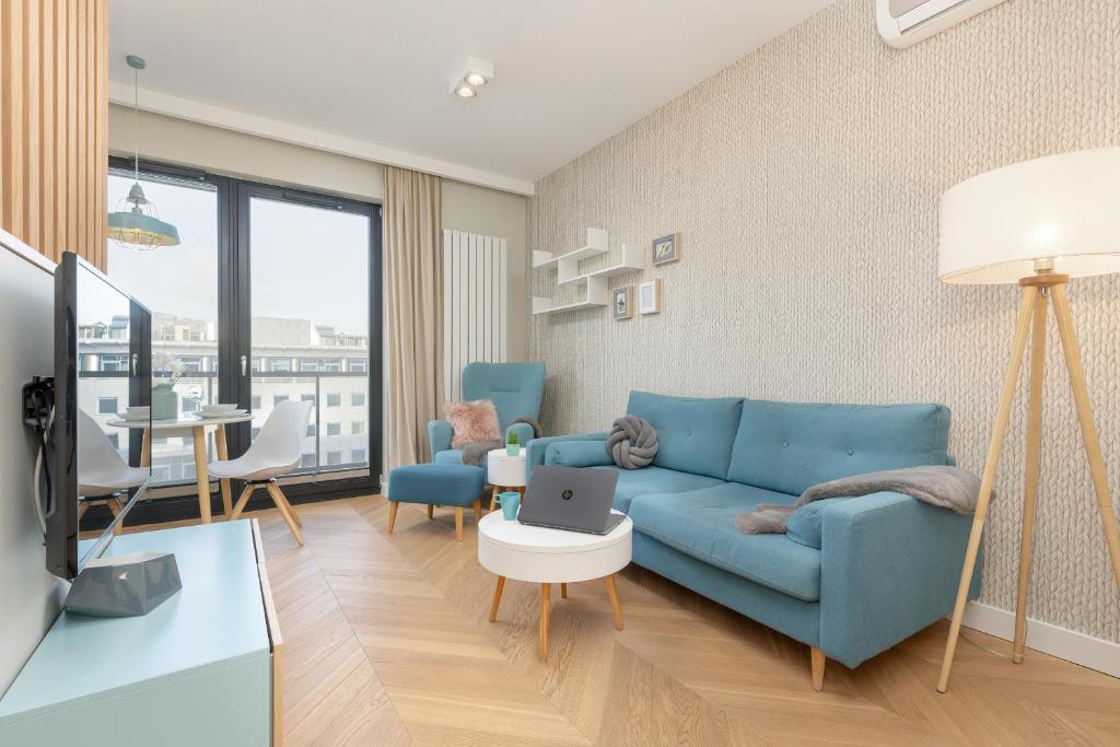 ein Wohnzimmer mit einem blauen Sofa und einem Tisch mit einem Laptop in der Unterkunft Bright Blue Apartment with Balcony, Parking and Air Conditioning in Warsaw by Renters in Warschau