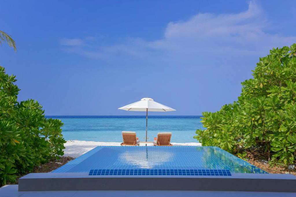 a pool with two chairs and an umbrella and the ocean at Emerald Faarufushi Resort & Spa - Deluxe All Inclusive in Raa Atoll