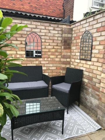 een patio met 2 stoelen, een tafel en een bakstenen muur bij Almond Cottage Clare - 2 bedroom English Cottage in Clare