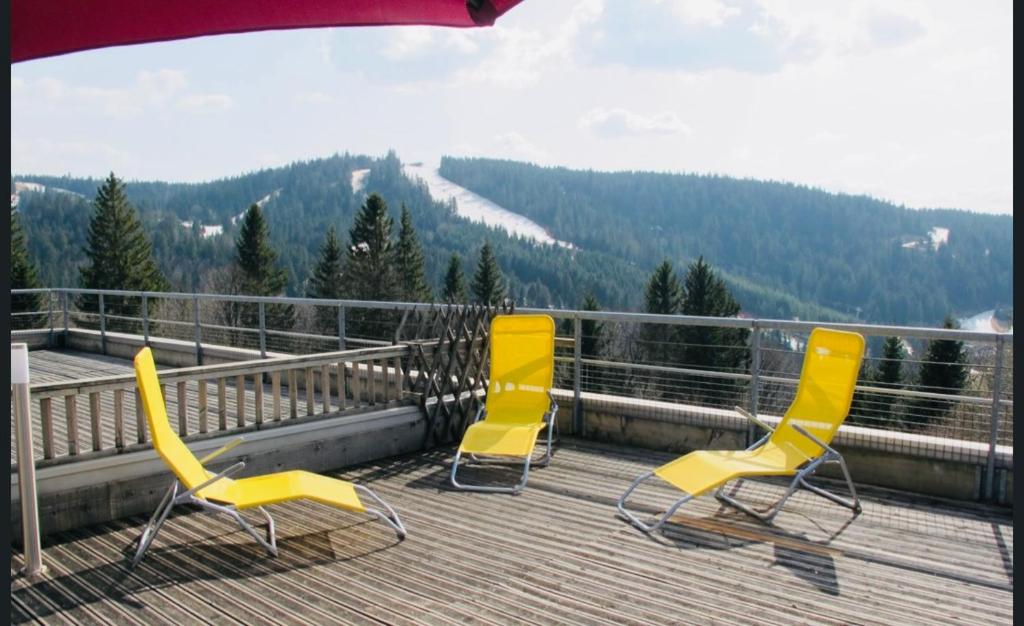 trois chaises jaunes assises sur une terrasse avec vue dans l'établissement Appartement sur les hauteurs de Gérardmer, à Gérardmer
