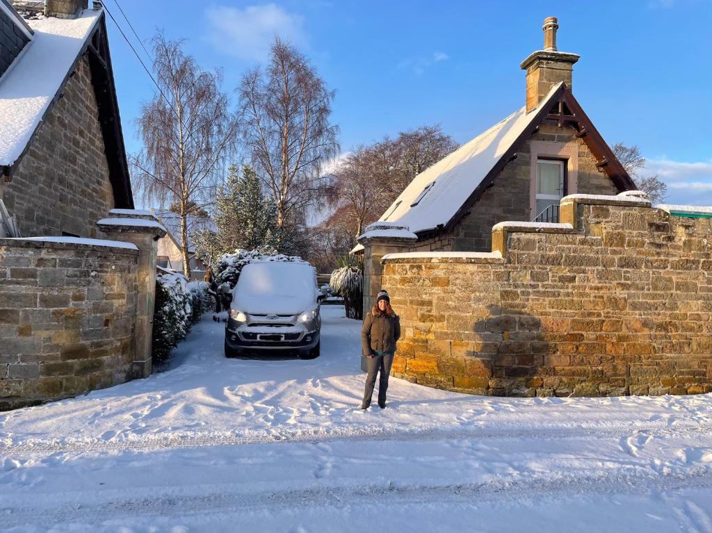 a woman standing in the snow in front of a house at Braemorriston Lodge in Elgin