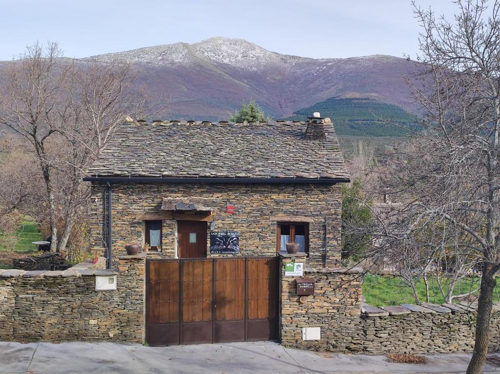 a stone house with a wooden gate and a mountain at Casa rural La Gata in Campillo de Ranas