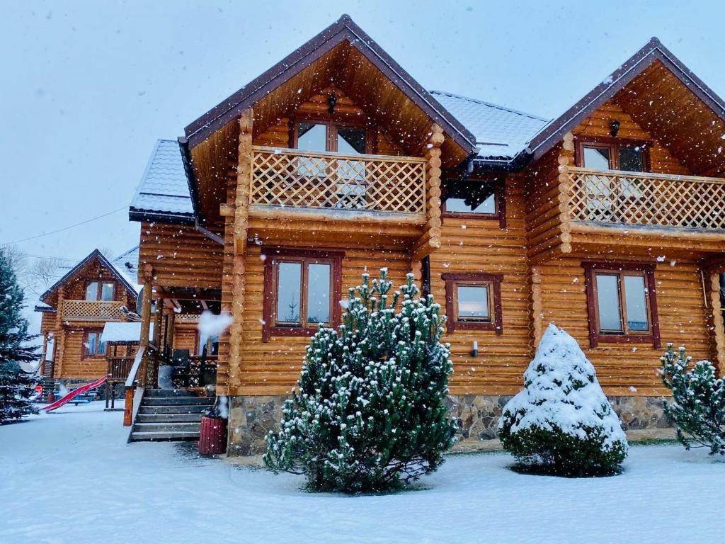 Cabaña de madera con nieve en el suelo y las ventanas en Садиба Панська, en Plavie
