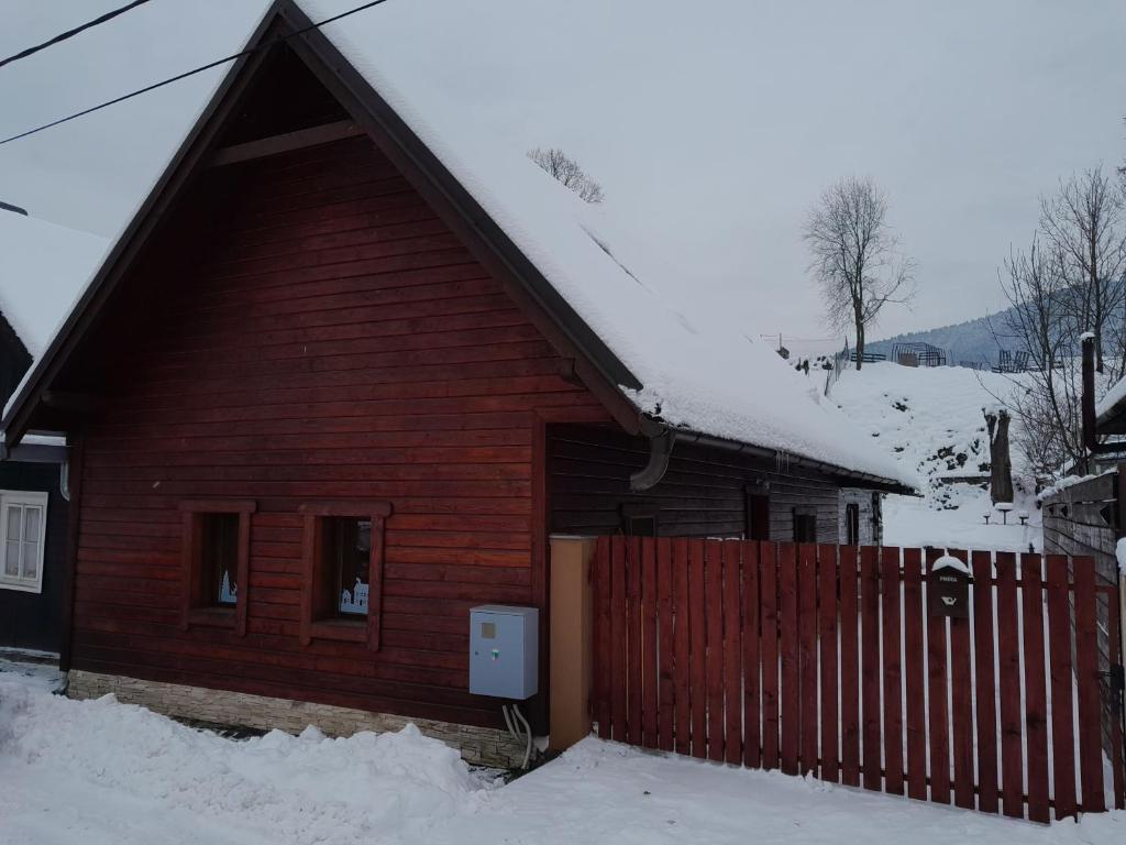 una cabina in legno con una recinzione rossa nella neve di Domček KaMi a Kráľová Lehota