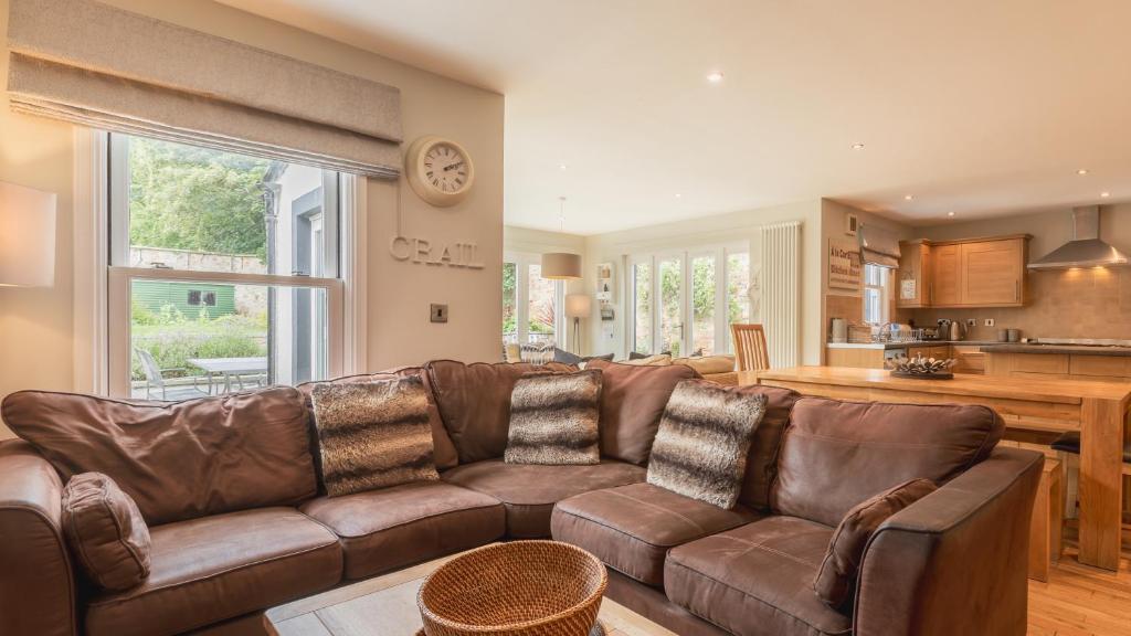 a living room with a brown leather couch and a kitchen at Garden Cottage, Crail in Crail