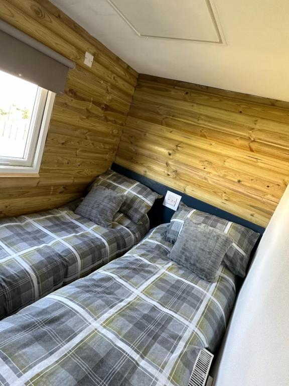 two beds in a room with wooden walls at Tracey’s Hideaway - with hot tub & amazing views in Llanasa