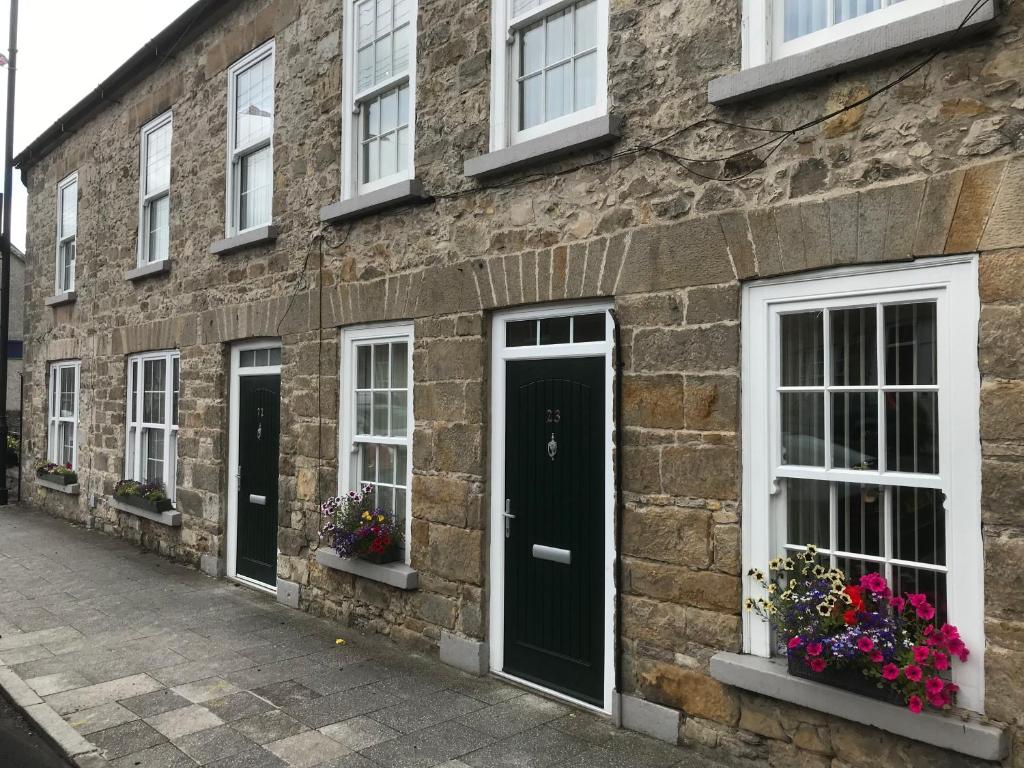 ein Backsteingebäude mit weißen Fenstern und grünen Türen in der Unterkunft Wee Betty’s Cottage in Caledon