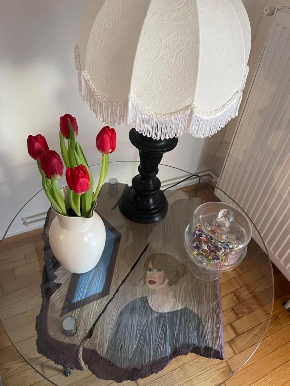 a table with a lamp and a vase with red flowers at Comfortable apartment in Thessaloniki in Thessaloniki