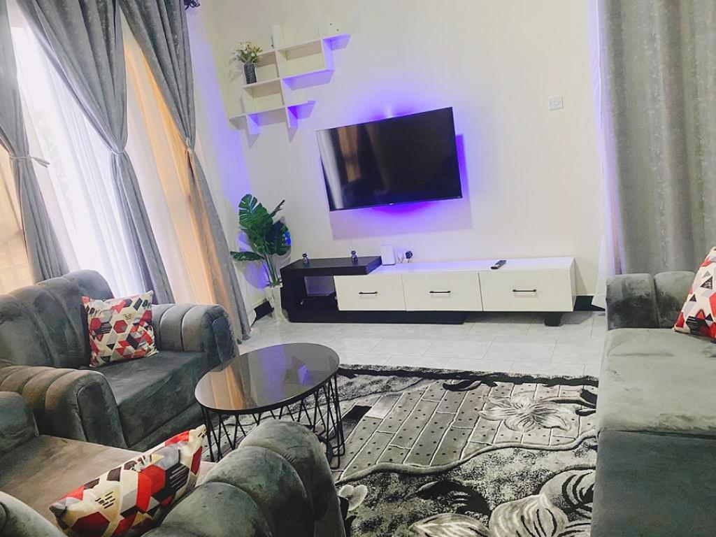 uma sala de estar com um sofá e uma televisão na parede em Kyaliwajala Heights Apartment em Kampala
