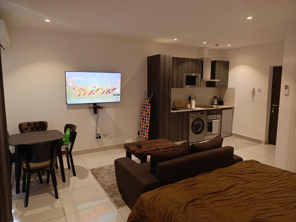 uma sala de estar com uma cama e uma televisão na parede em Just Nice Stays @ The Gardens em Acra