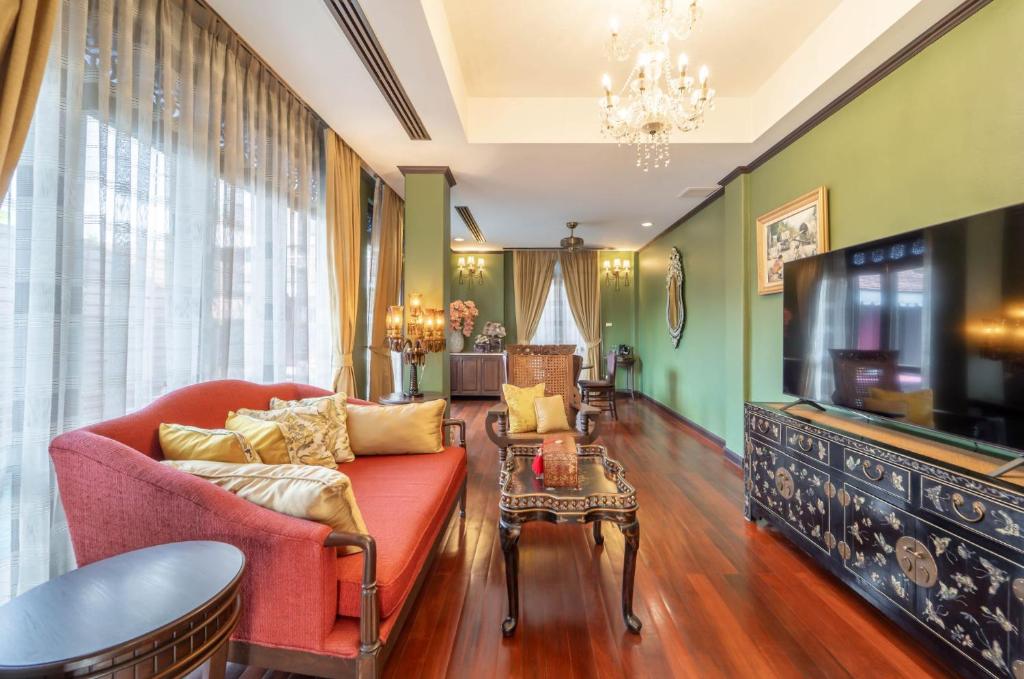 A long living room with a red sofa, television, dining table, and chandelier.