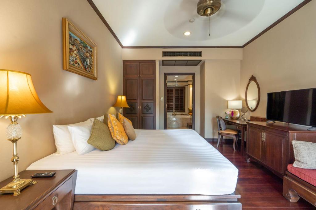 A warmly styled bedroom with a large white bed, television and traditional wood furnishings.