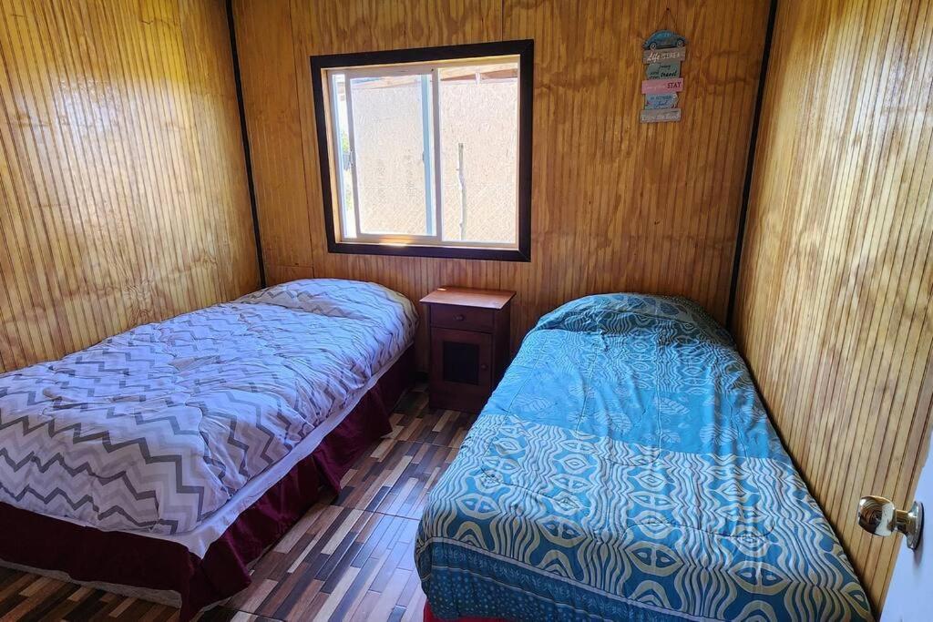 2 Betten in einem kleinen Zimmer mit Fenster in der Unterkunft Cabaña buck in Dalcahue