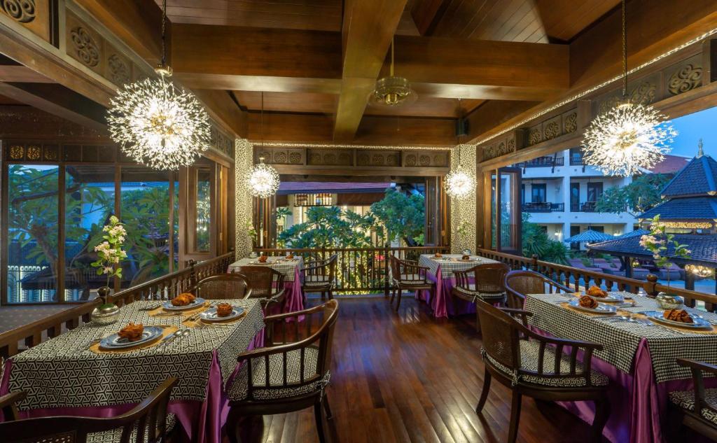 An evening dining room with chandeliers, dark wood interiors and a balcony-like garden outlook.