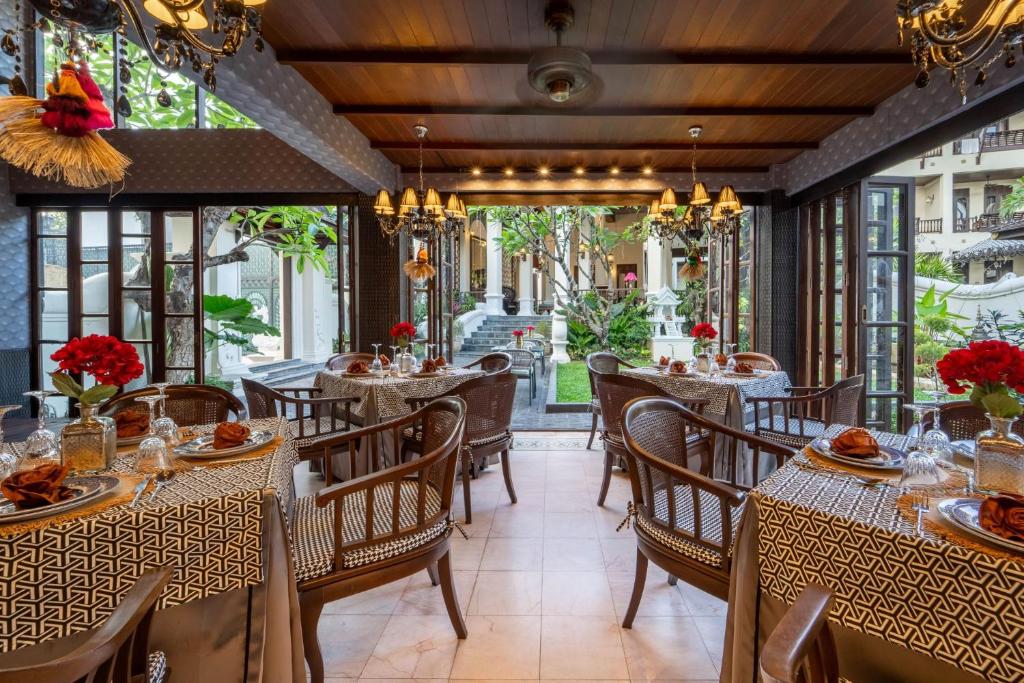 A bright, garden-facing dining room with open windows, set tables and traditional chandeliers.