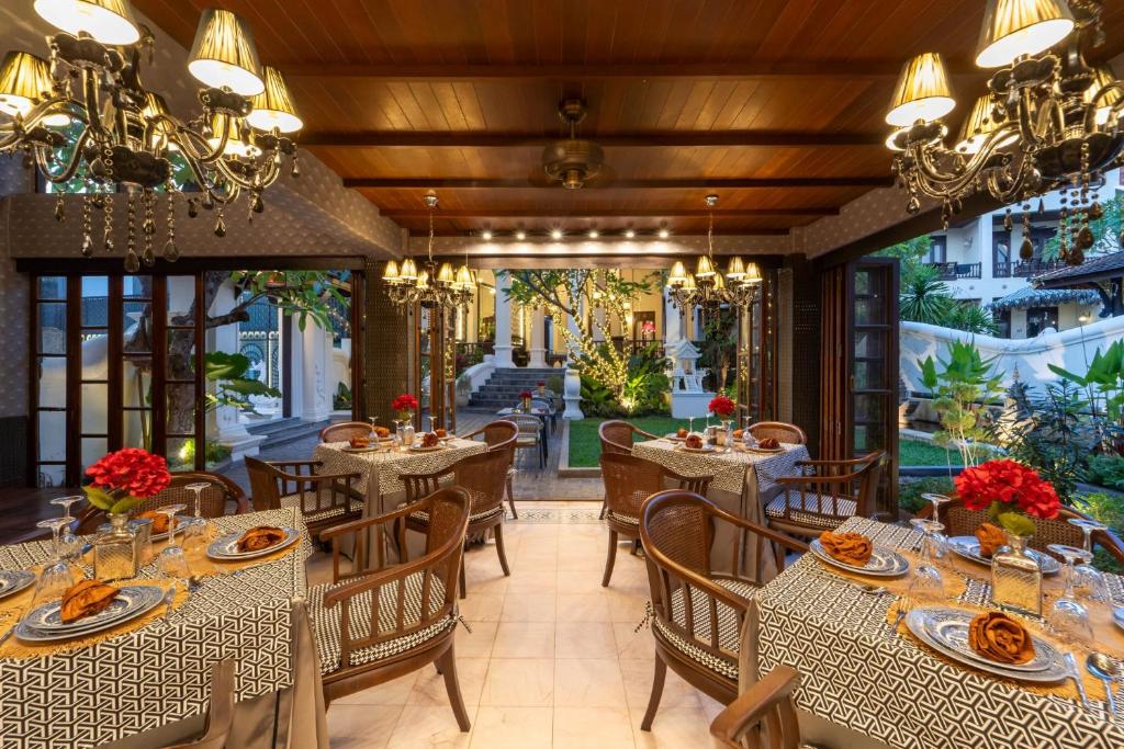 A formal dining room with set tables, wicker chairs, chandeliers and garden-facing openings.