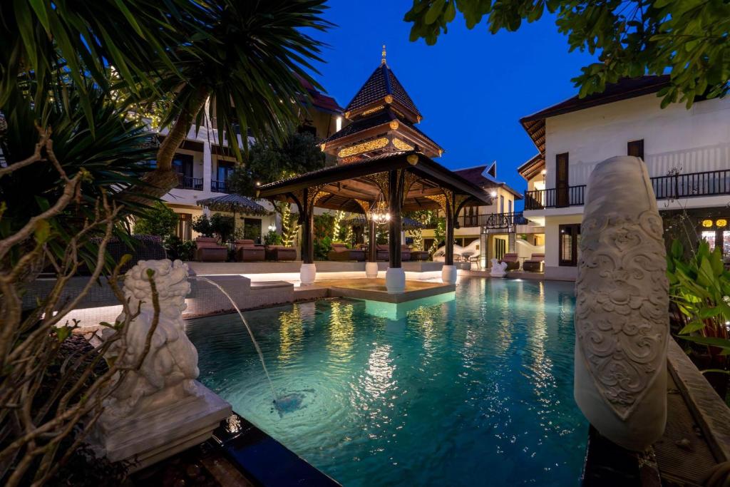 An illuminated courtyard pool beneath a Thai-style pavilion at dusk.