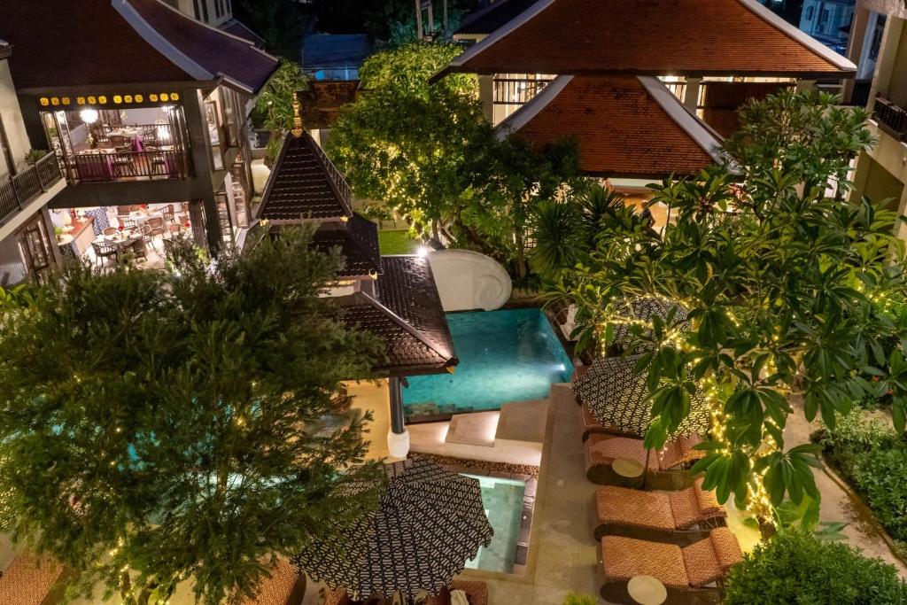 An elevated evening view over a small garden pool surrounded by tiled roofs, trees and loungers.