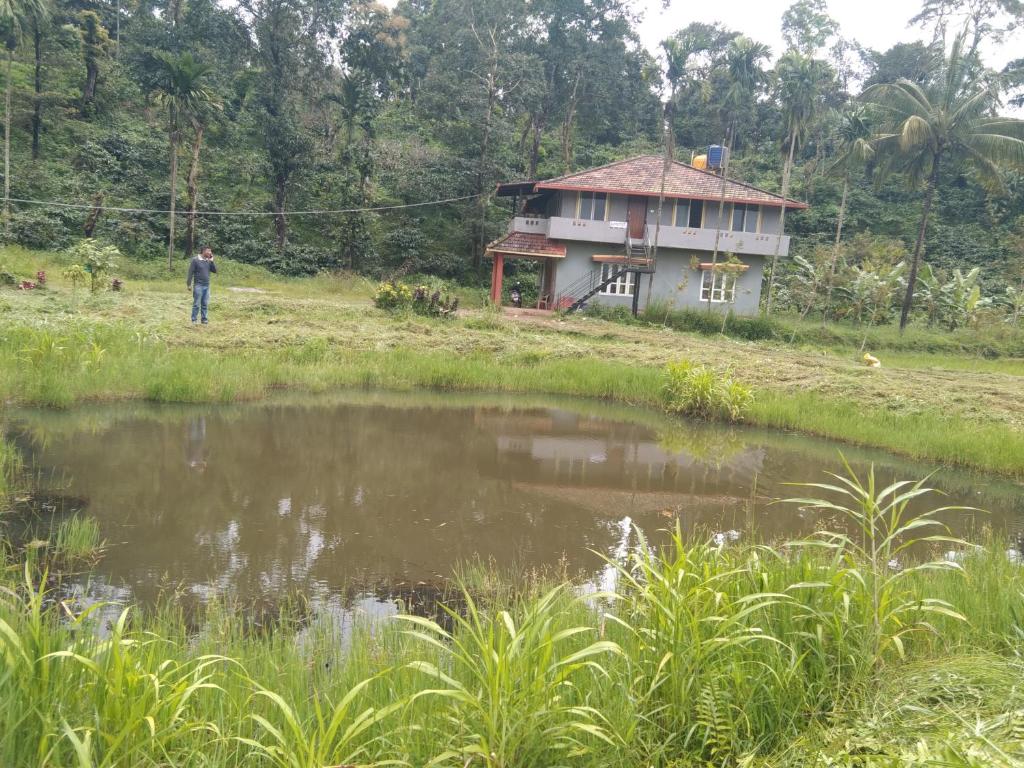 un homme debout devant une maison à côté d'un étang dans l'établissement Samz estate stay 2BHK, à Madikeri