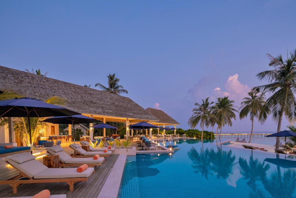 una piscina en un complejo con tumbonas y sombrillas en Emerald Faarufushi Resort & Spa - Deluxe All Inclusive, en Raa Atoll