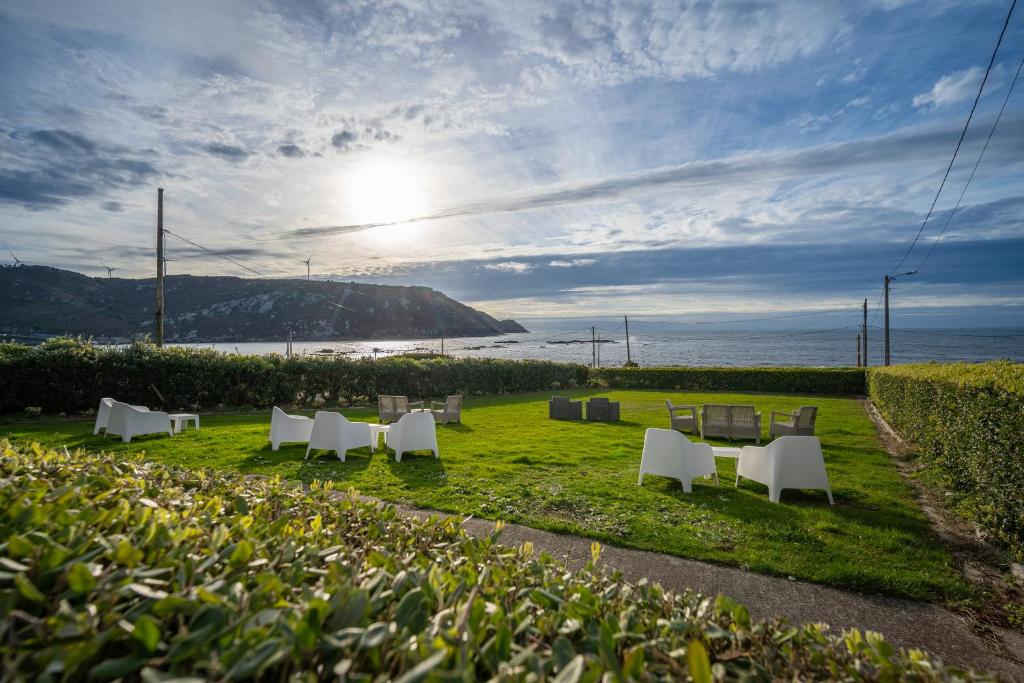 eine Reihe weißer Stühle auf einem Feld mit dem Meer in der Unterkunft Casa da Vasca in Malpica