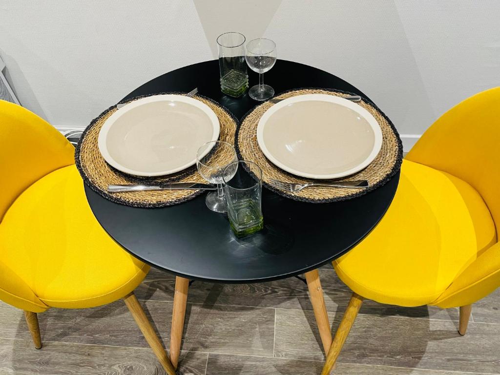 uma mesa preta com cadeiras amarelas, pratos e copos em Studio cosy 