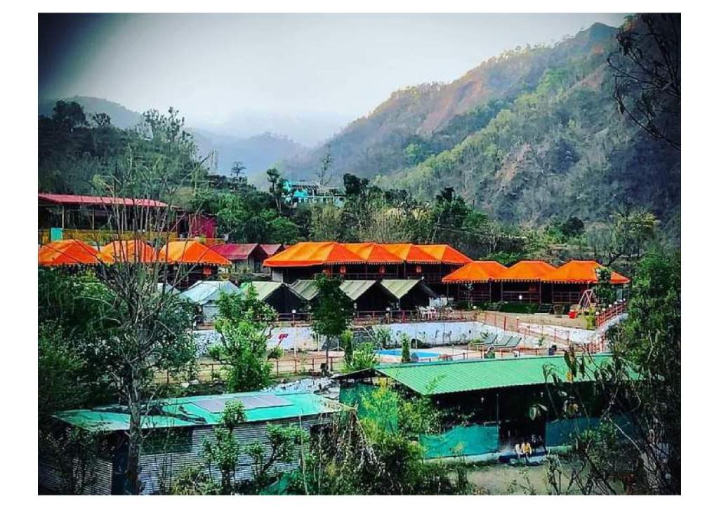 a group of buildings with orange roofs next to a mountain at Anandam Camping in Rishīkesh