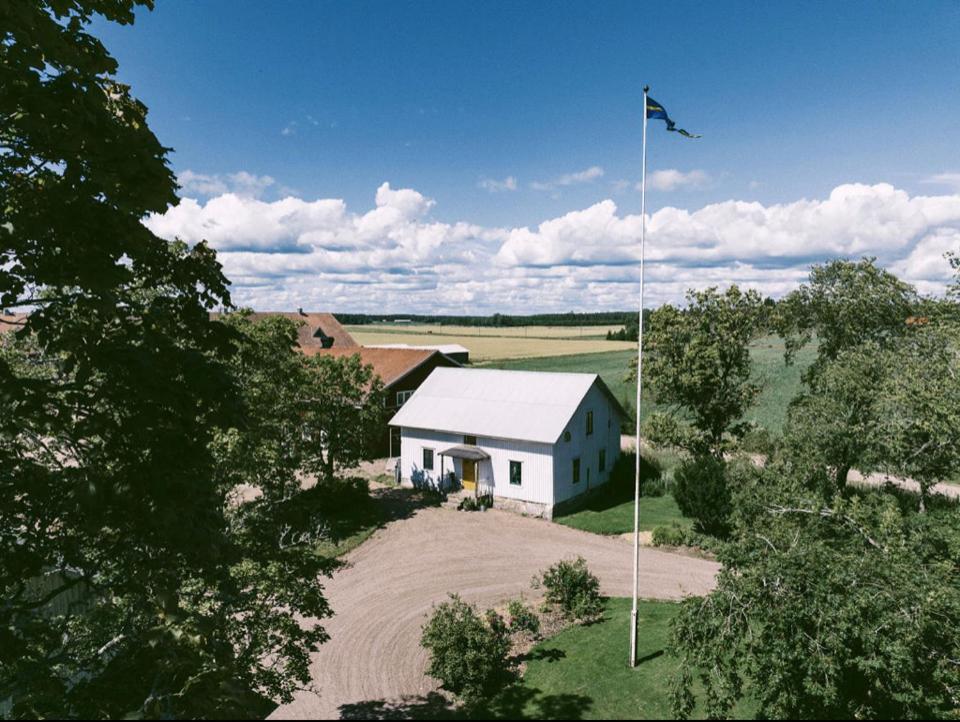 克里斯蒂娜港的住宿－Åkerbo gård charmigt renoverad flygel，一块带旗帜的田野中间的白色房子