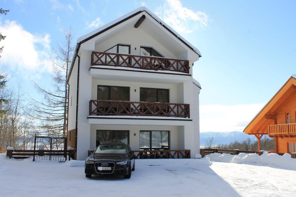 a white house with a car parked in the snow at Hellene Snow Starý Smokovec in Vysoke Tatry - Stary Smokovec
