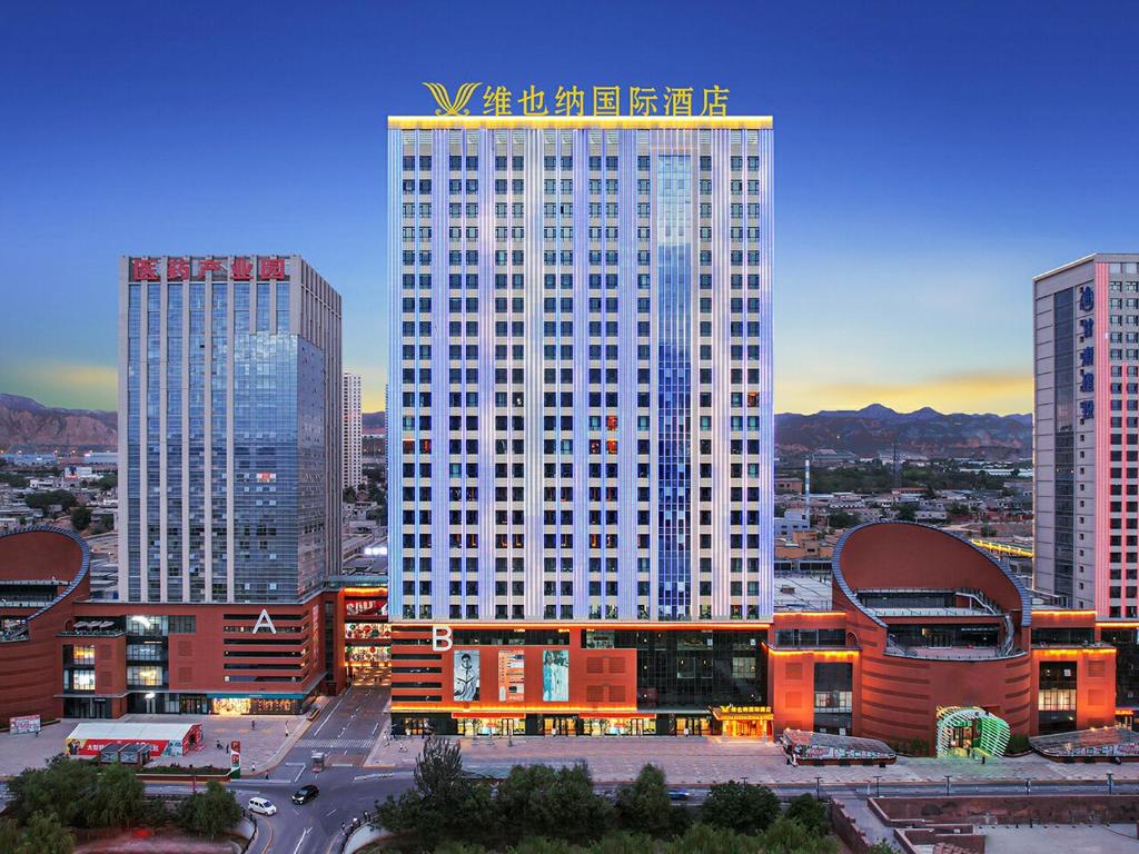 a large white building in a city with tall buildings at Vienna International Hotel Lanzhou SASSEUR Outlets & Yellow Riverside in Lanzhou