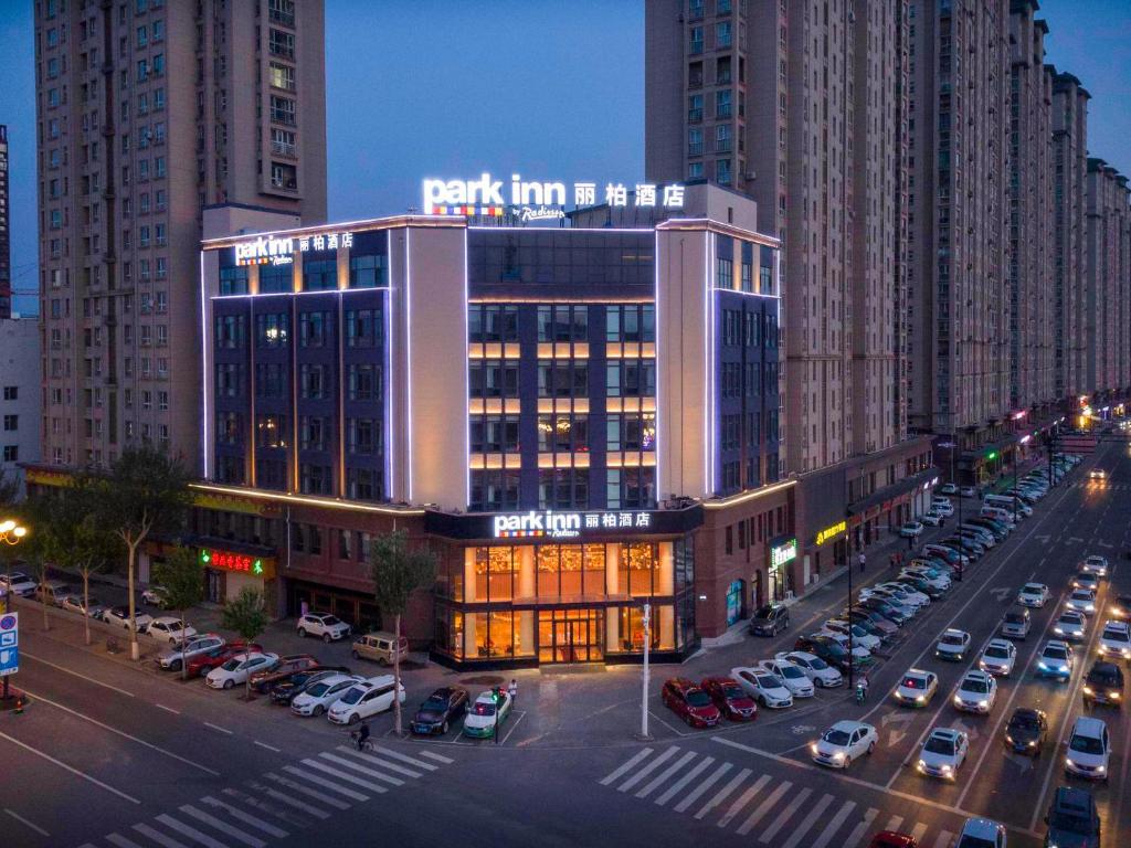 un grand bâtiment avec des voitures garées dans un parking dans l'établissement Park Inn by Radisson Jilin Beishan Park&Songhua River, à Jilin