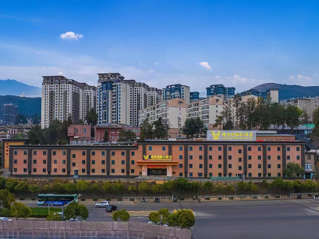 a large building in front of a city with tall buildings at Vienna International Hotel Kunming longquan road Finance University in Kunming