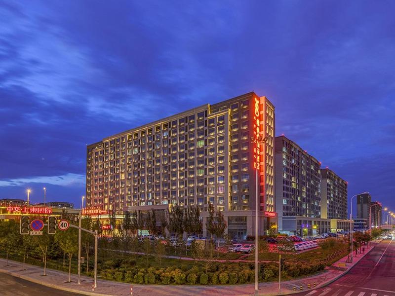 un grand bâtiment avec des lumières rouges sur son côté dans l'établissement Vienna International Hotel Hohhot High Speed Railway East Station, à Hohhot