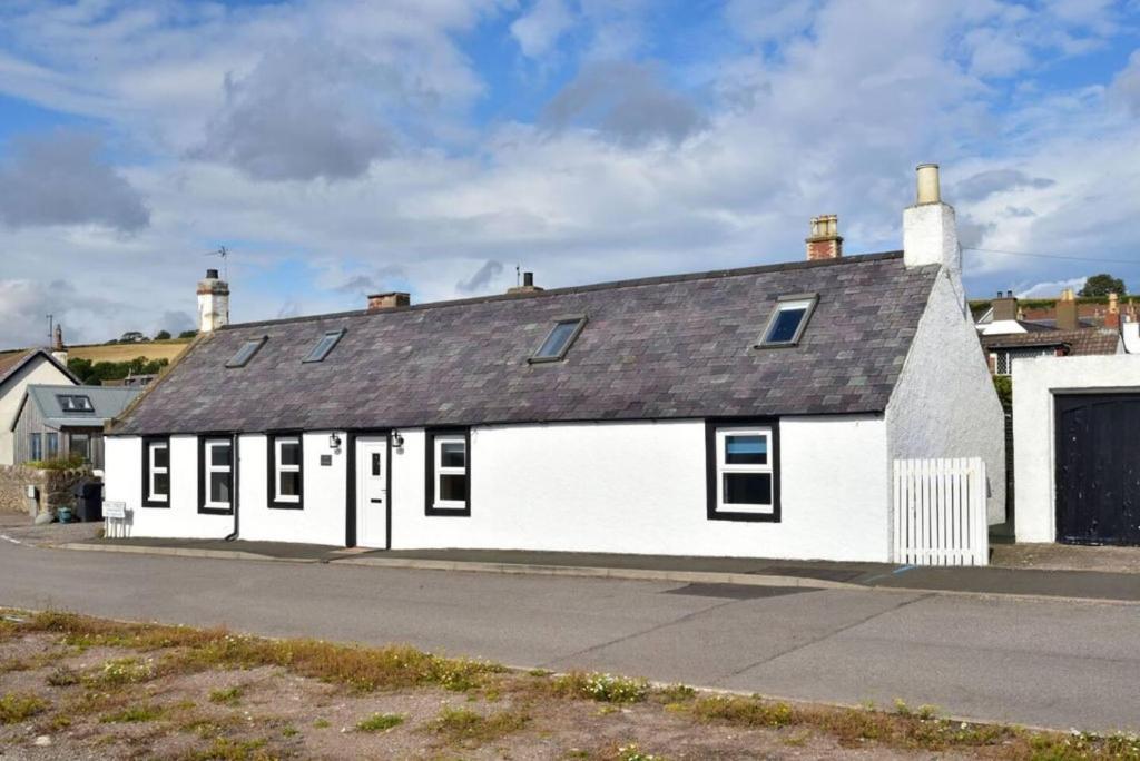 a white building with a black roof on a street at Impeccable 2-Bed Cottage in Johnshaven in Montrose