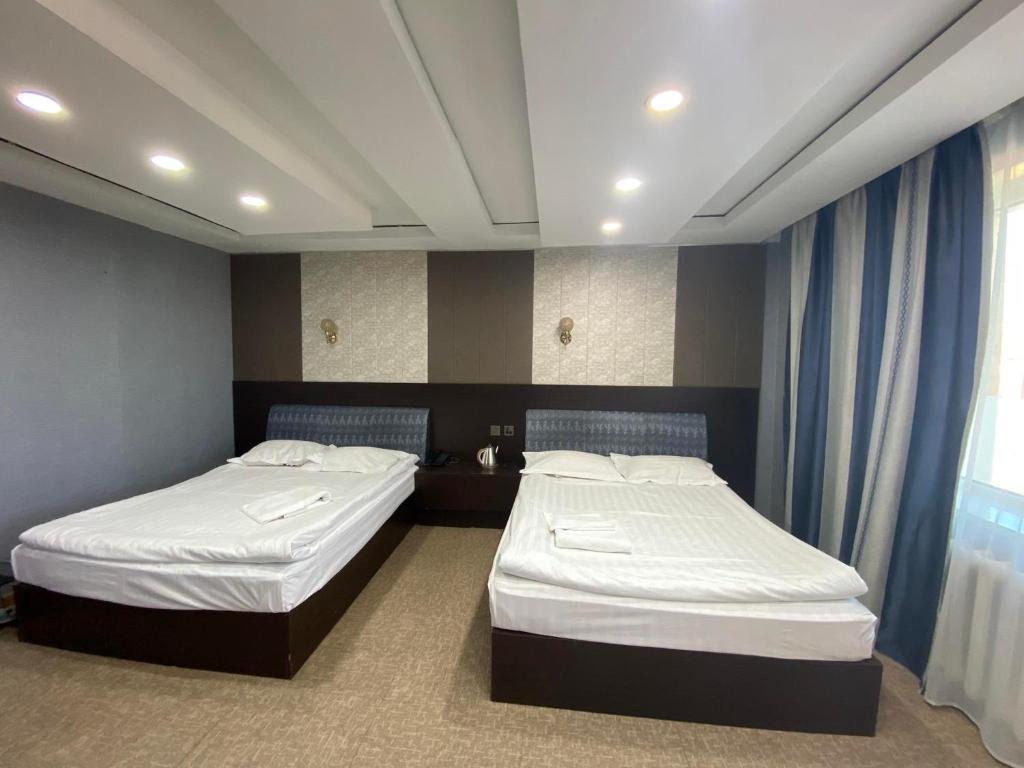 two twin beds in a room with blue curtains at Jasper Hotel in Darhan