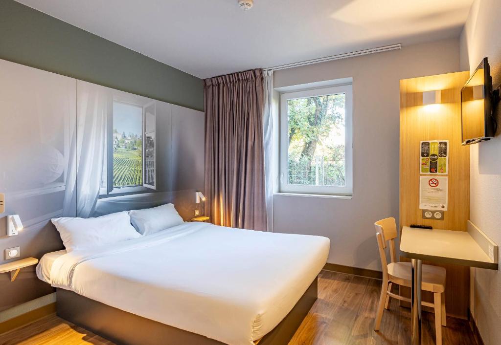 a bedroom with a bed and a desk and a window at B&B HOTEL Bordeaux Langon in Langon