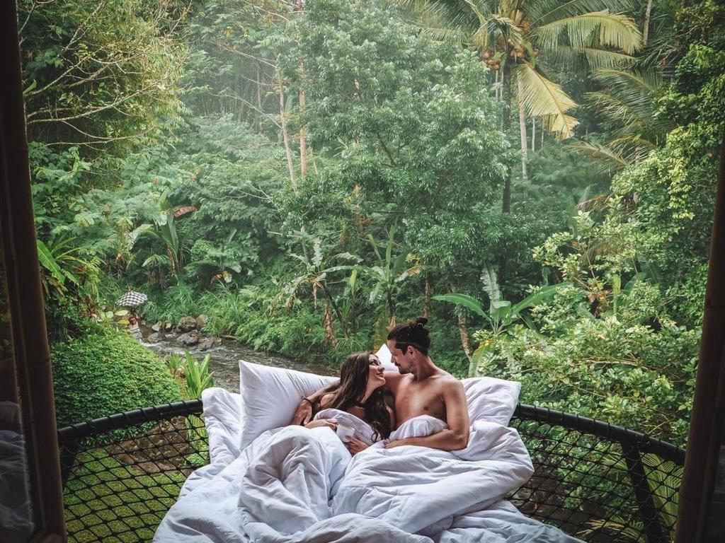 un hombre y una mujer acostados en una cama con un bebé en Eco Bamboo Island Bali - Bamboo House #3, en Selat