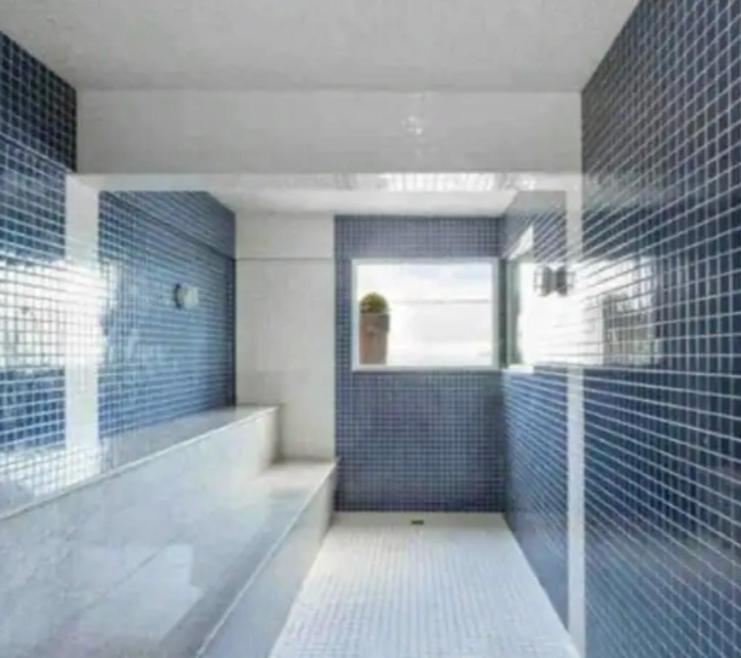 ein Bad mit blau gefliesten Wänden und einer ebenerdigen Dusche in der Unterkunft Macaé Ramada Flat RJ in Macaé