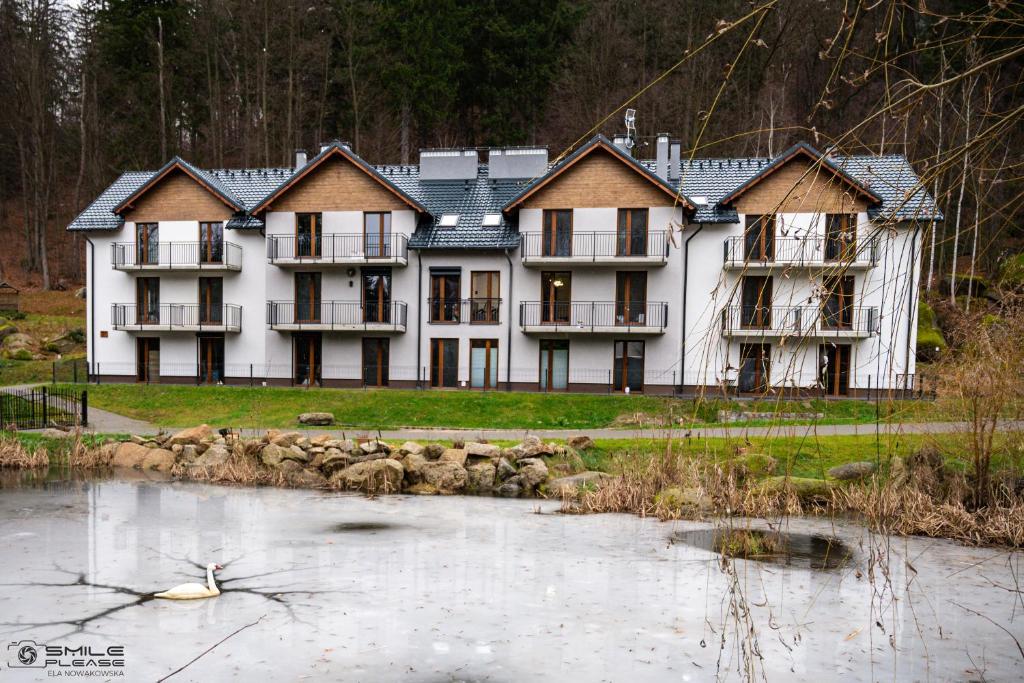 ein großes weißes Gebäude neben einem Wasserkörper in der Unterkunft Apartamenty Nad Potokiem koło Karpacza in Staniszów