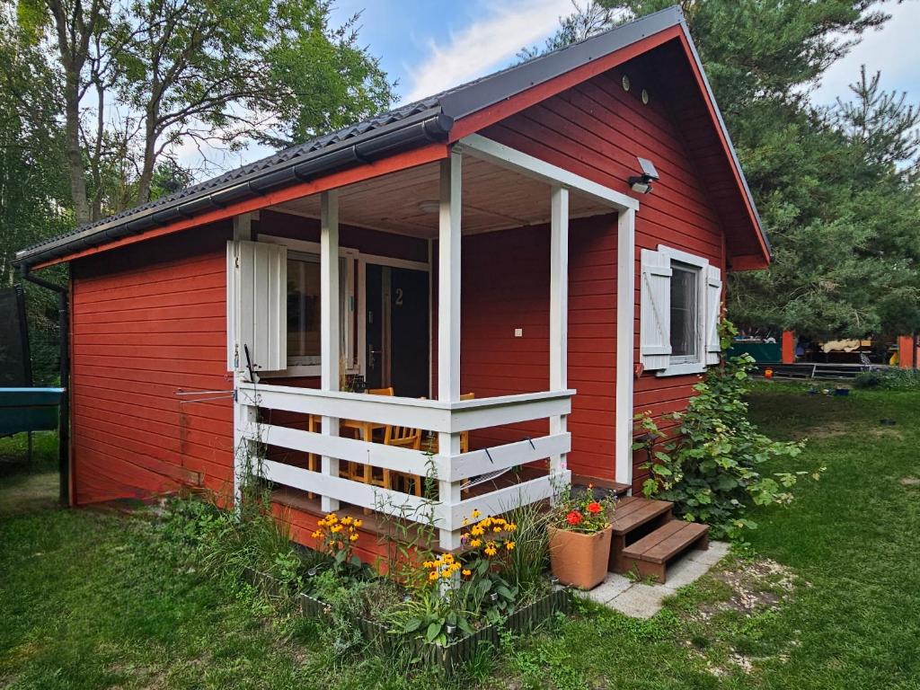 une maison rouge avec une terrasse couverte et des fleurs dans la cour dans l'établissement Czerwone Domki Wartowo, à Kołczewo