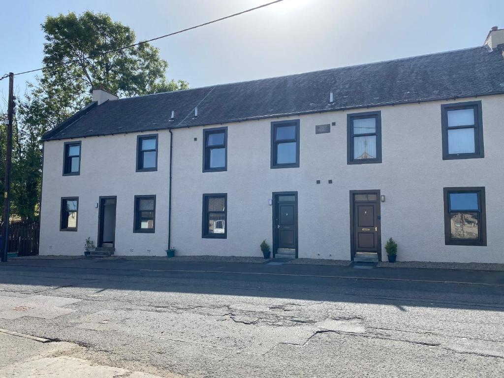 a white house with black windows and doors on a street at Welltrees Apartments 14 Dailly Road Maybole in Maybole