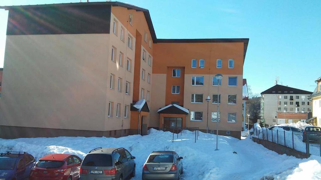 un groupe de voitures garées dans la neige devant un bâtiment dans l'établissement Apartmán U kostela, à Železná Ruda